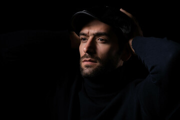 A thoughtful man wearing a black turtleneck and cap, captured in a low-key dramatic lighting...