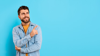 Smiling confident young man points aside on blue background, panorama
