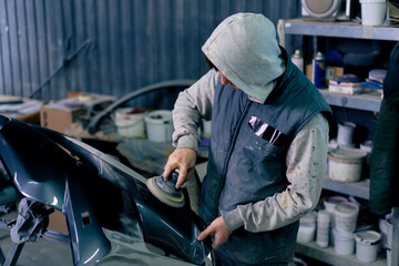 auto mechanic at a service station polishing the front part of dark blue car
