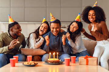 guy making wish on birthday celebration surrounded by friends indoor