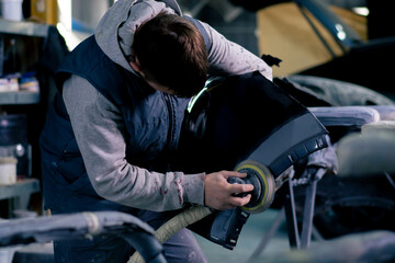 auto mechanic at a service station polishing the front part of dark blue car - obrazy, fototapety, plakaty
