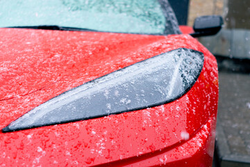 close-up the headlights of a light red sports car standing on the street wet after the snow