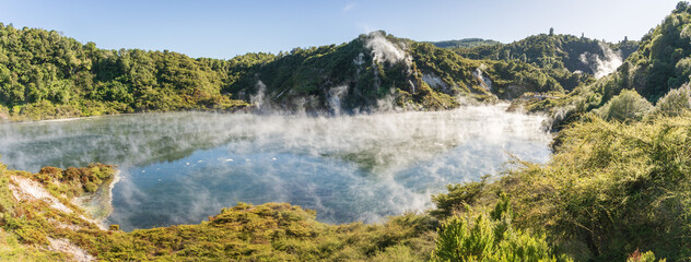 Panoramic view on huge boiling geothermal lake surrounded by lush green foliage, New Zealand