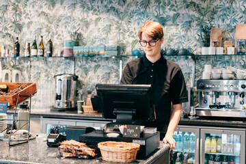 Young waiter serving customer at cash point in cafe. Man working with POS terminal. Cashier,...