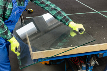 Glass factory, glazier places a heavy glass panel on a professional cutting table