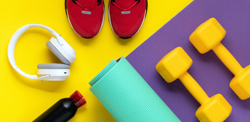 Dumbbells on purple roll mat on yellow background. Sport lifestyle concept. Flat lay. Red sneakers,...