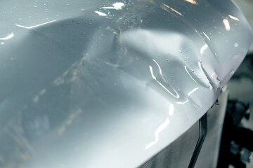 close-up of a part of a silver car bent after an accident before straightening at service station