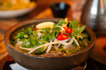 Vietnamese Pho soup in a bowl, topped with fresh herbs, chili, and lemon on a rustic table