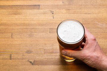 Hand Holding a Pint of Craft Beer on Wooden Table