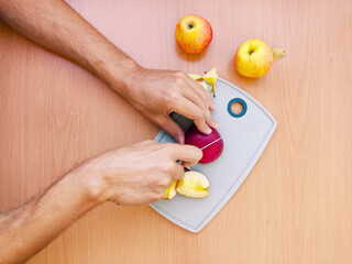 Close up male hands cut an apple into slices. Top view of preparing fruits over kitchen table.
