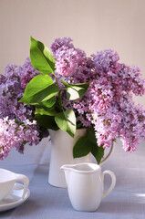 still life with white dishes on the table and a bouquet of lilacs