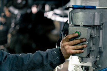 A car mechanic stands at a service station and presses button on a pole to raise the car