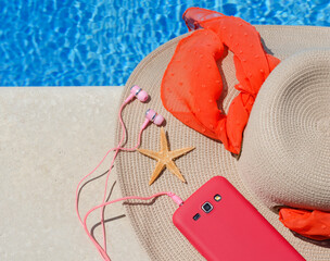 Women's raffia hat, telephone and starfish next to the pool