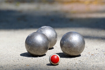 Petanque balls are placed near a target ball on an outdoor dirt field, where 12 round metal balls are thrown as close as possible to the target team that reaches 13. The first to score is the winner.
