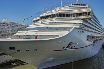 Huge cruiseship or cruise ship liner in port at terminal with skyline and shore view under blue sky ready for cruising	