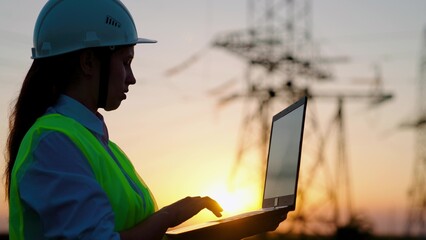 Woman engineer, power engineer in helmet checks power line using computer laptop online....