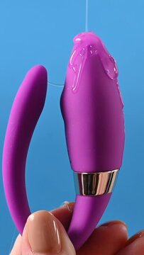 A woman holds a curved sex toy in lubrication on a blue background.  Vaginally clitoral vibrator. Vertical video.