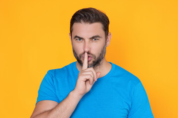Shh man. Portrait of man showing shh taboo sign with finger to lips over yellow studio background. The secret. Hush shut silent Concept. Mute and quiet, finger on mouth shush sign. Silence gesture.