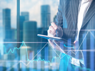 Financial specialist. Economic charts near trader with tablet. Cropped investor. Trader makes investment transaction. Businessman trading in stock exchange app. Trader near blurred skyscrapers - obrazy, fototapety, plakaty