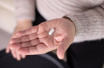 Wrinkled palms of mature woman with painkiller headache pills on blurred background. Female person shows effective medication to fight pain closeup.