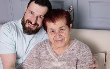 Family, generation and people concept - happy smiling senior mother with adult son hugging at home.