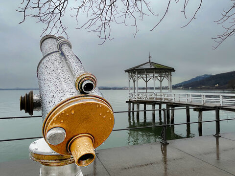 A telescope covered with raindrops, in the background the former fishing pier in Bregenz on Lake Constance.