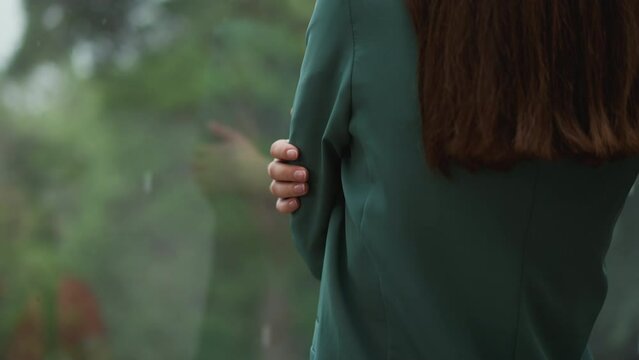 Woman stands by window on rainy day closeup. Frozen businesswoman self hugs spending time on terrace. Lady contemplates nasty weather in office