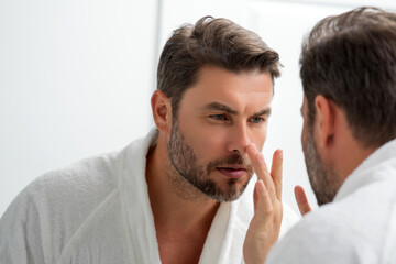Fototapeta premium Beauty face portrait of a beautiful man applying face cream. Moisturizing skincare cream for man. Mask, skin lifting and anti-aging effect. Beauty male face concept. Skincare and aging. Face cosmetic.
