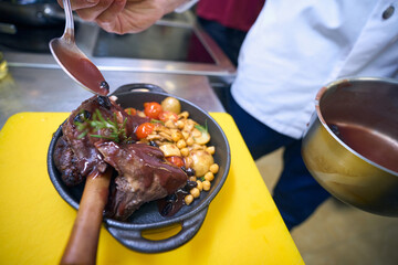 Cook prepares meat with vegetables and sauce for serving