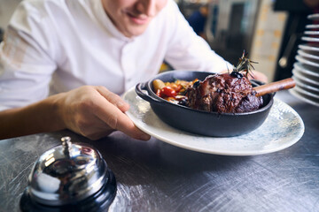 Young kitchen employee has prepared lamb shank with vegetables for serving