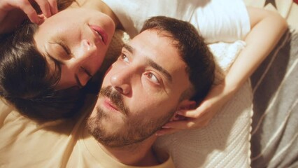 Young beautiful girlfriend and boyfriend lying head to head on bed, touching each other with affection and having a talk. Close-up shot, top down view