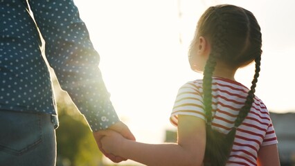 Smiling cute baby daughter and caring mother walking together holding hands summer park sun light...