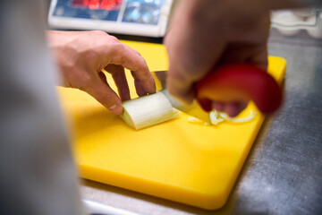 Cook chops an onion on a yellow cutting board