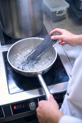 Cook puts a portion of black spaghetti into boiling water
