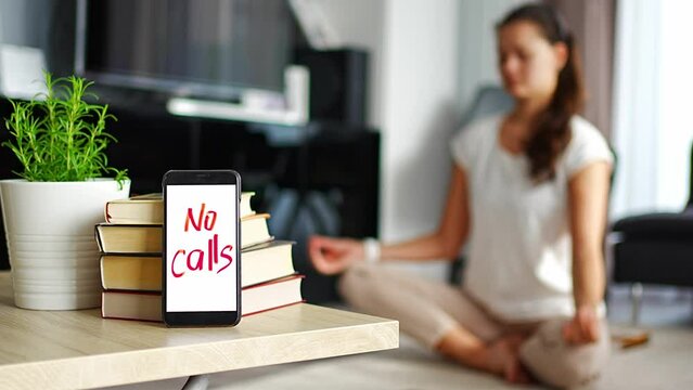 Digital detox concept. In the foreground is a smartphone with the text No Calls and woman meditating in the background. High quality 4k footage