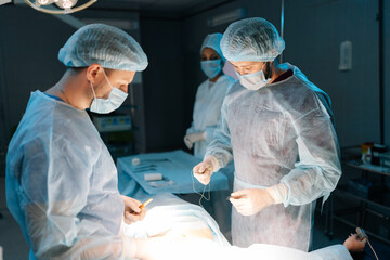 Skilled professional surgeons and nurse in uniform at work in operating room, performing heart transplant surgery operation under bright lamps. Teamwork surgeon in operating room.