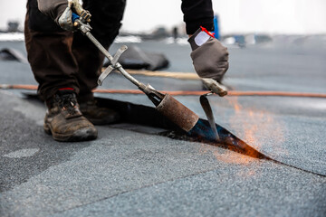 professional roofer applying bitumen roll on flat roof with a gas burner at a modern construction...
