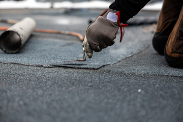 professional roofer applying bitumen roll on flat roof with a gas burner at a modern construction site - obrazy, fototapety, plakaty
