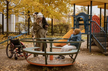 Fototapeta na wymiar a 10-year-old boy in a wheelchair walks in the fall with his mother on the street with a dog on the playground. High quality photo
