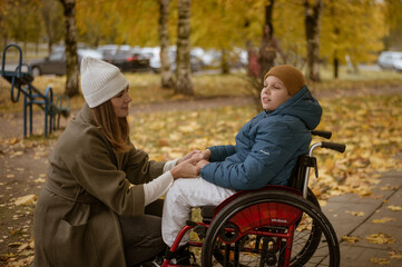 a 10-year-old boy in a wheelchair walks in the fall with his mother on the street with a dog on the playground. High quality photo
