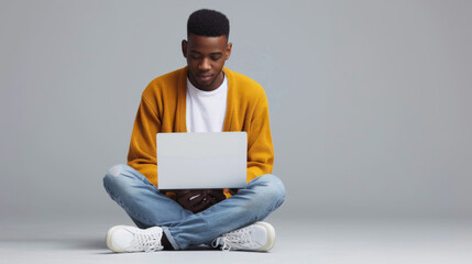 A person is sitting cross-legged on the floor, focused on working with a laptop.