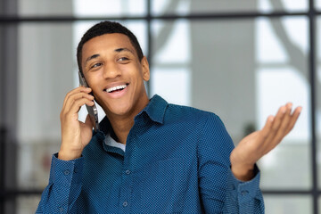 Young African American business man talking on a mobile phone in his workplace standing in a modern office