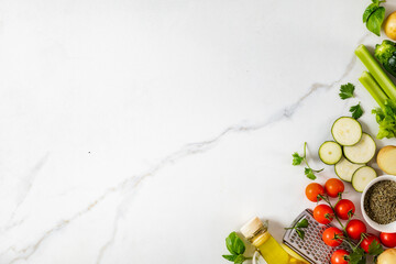 Healthy food cooking ingredients background with fresh vegetables, herbs, spices and olive oil on marble table with copy space top view