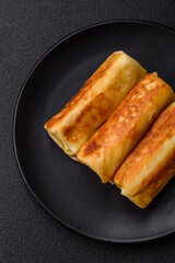 Delicious fried pancakes with filling rolled on a dark concrete background