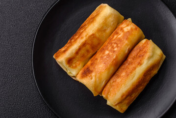 Delicious fried pancakes with filling rolled on a dark concrete background