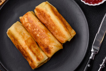 Delicious fried pancakes with filling rolled on a dark concrete background