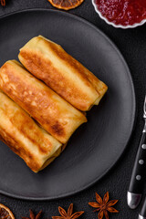 Delicious fried pancakes with filling rolled on a dark concrete background