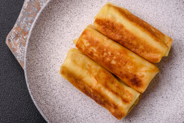 Delicious fried pancakes with filling rolled on a dark concrete background