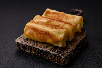 Delicious fried pancakes with filling rolled on a dark concrete background