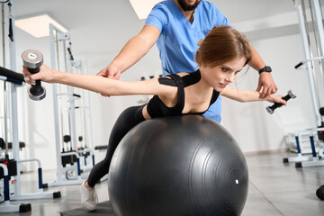 Beautiful woman performs exercises with a fitball and dumbbells